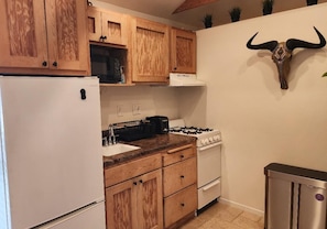 A kitchen with wooden cabinets, a white refrigerator, a gas stove, and a trash bin.