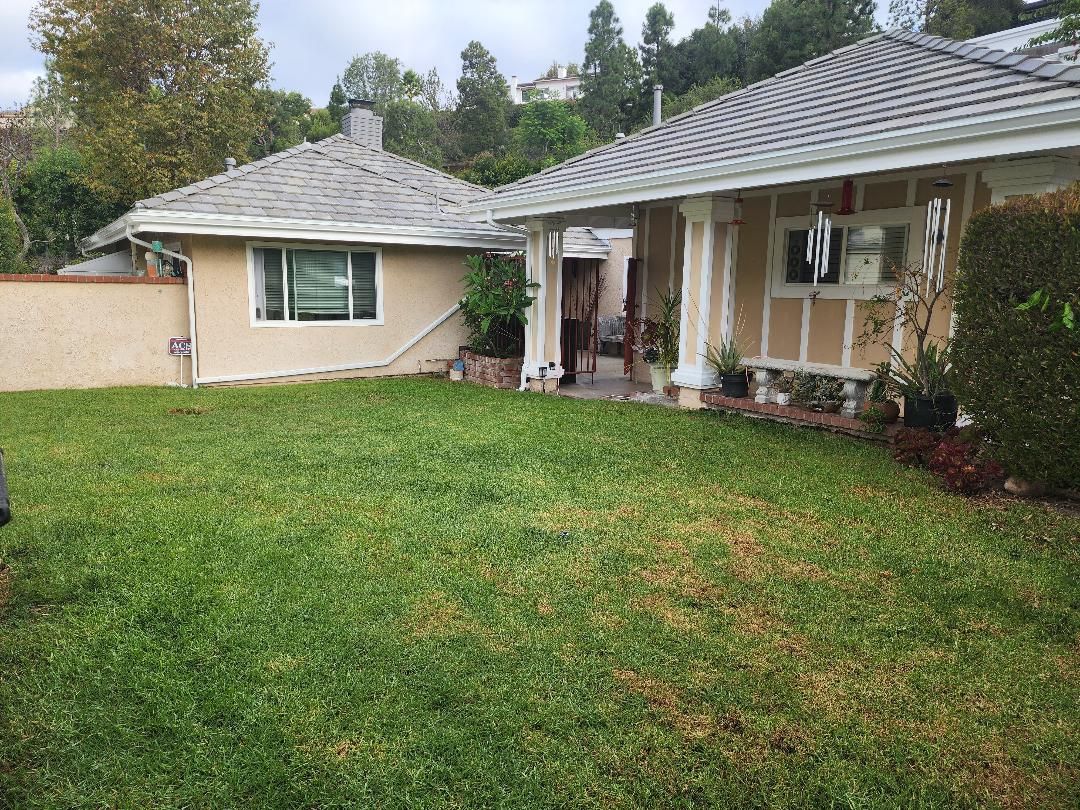 A residential property with a well-maintained lawn, a covered porch, and a two-story house with a tiled roof.