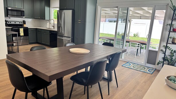 A modern kitchen with dark cabinets, stainless steel appliances, and a wooden dining table with chairs.