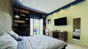 Un dormitorio con una cama grande, un escritorio, una estantería, un televisor y vistas al balcón.