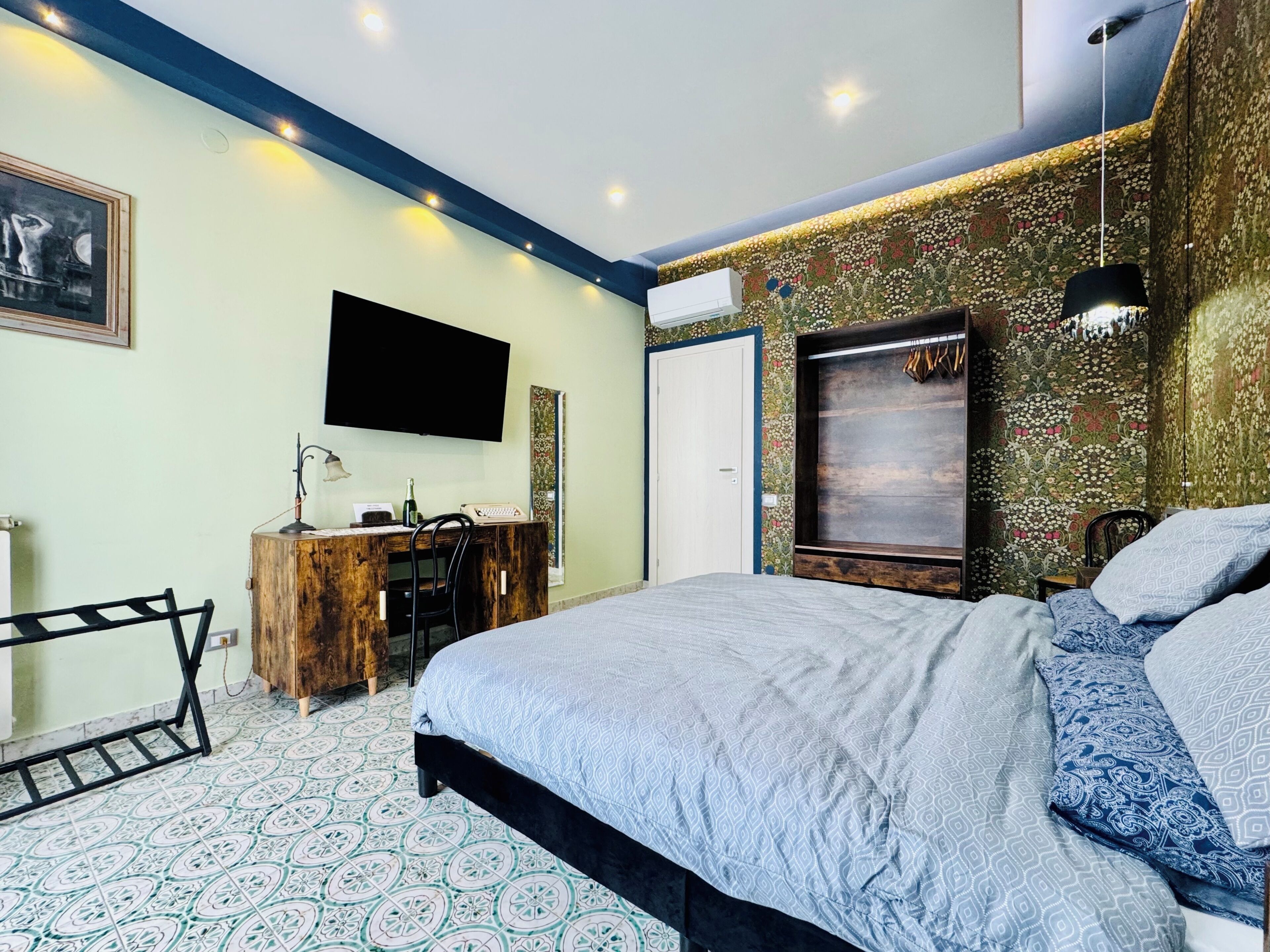 A bedroom with a bed, a desk, a chair, a TV, and an air conditioning unit.