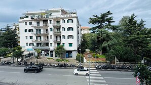 Un edificio residencial de varios pisos con balcones, un paso de peatones y vehículos estacionados.