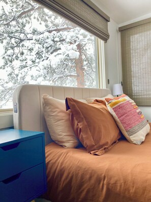 A bedroom with a bed, pillows, a nightstand, and a window with a view of snow-covered trees. - the Sheep Shack #6204 - Private Hot Tub - Mountain Views - 3 bedrooms - Fire Pit (Estes Park)