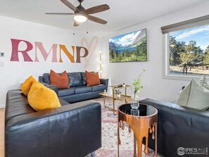 A modern living room with a black leather sofa, a round coffee table, and a large window with a mountain view. - the Sheep Shack #6204 - Private Hot Tub - Mountain Views - 3 bedrooms - Fire Pit (Estes Park)