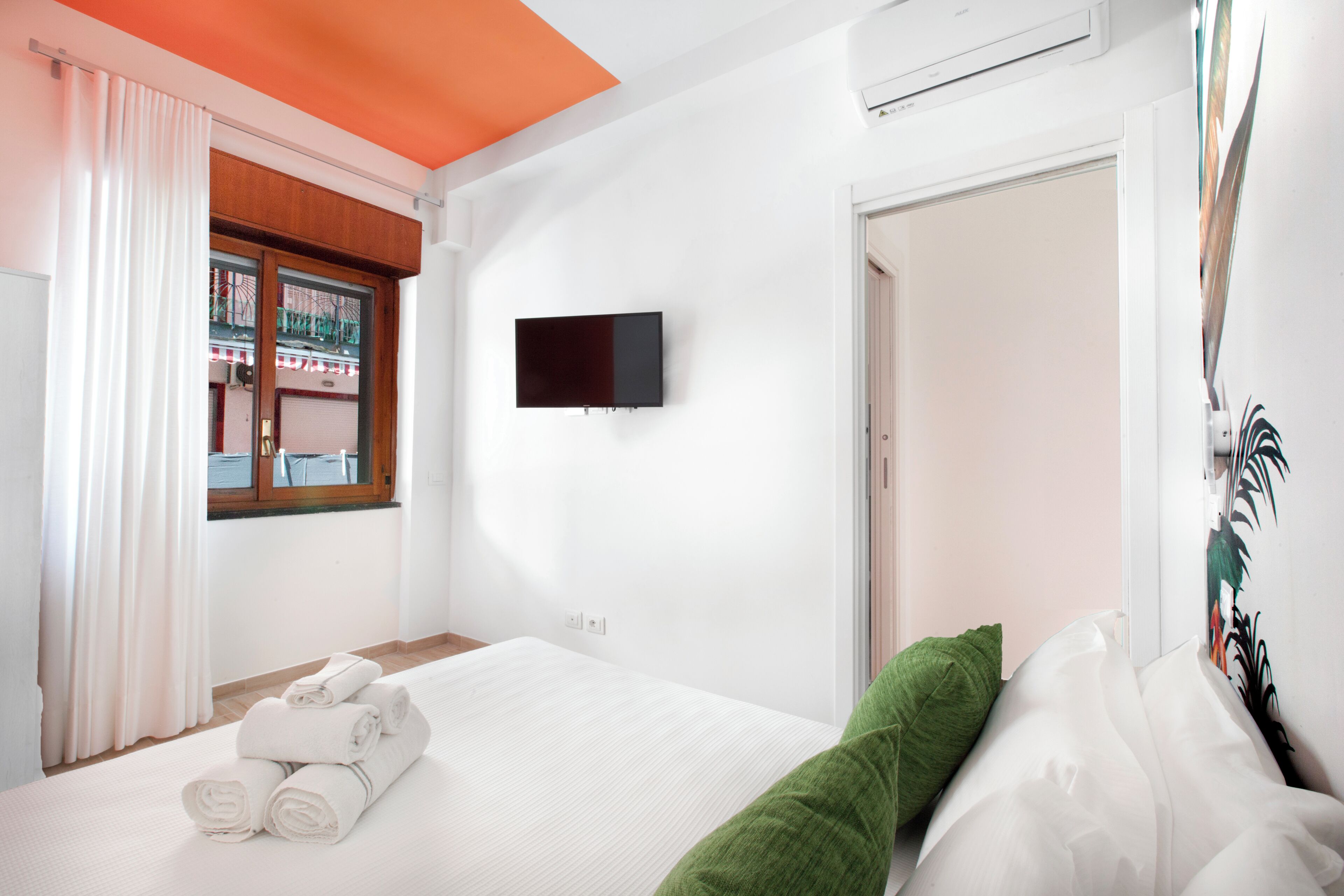A bedroom with a bed, a flat-screen TV, a window with curtains, and a door.
