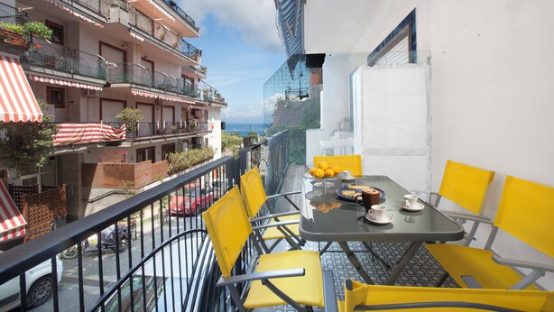 Ein Balkon mit gelben Stühlen und einem Tisch, mit Blick auf eine Straße mit parkenden Autos und einem Gebäude mit Balkonen.