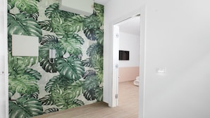 Ein Flur mit tropischem Blattmuster an der Wand, einer weißen Tür und einem hellen Boden.