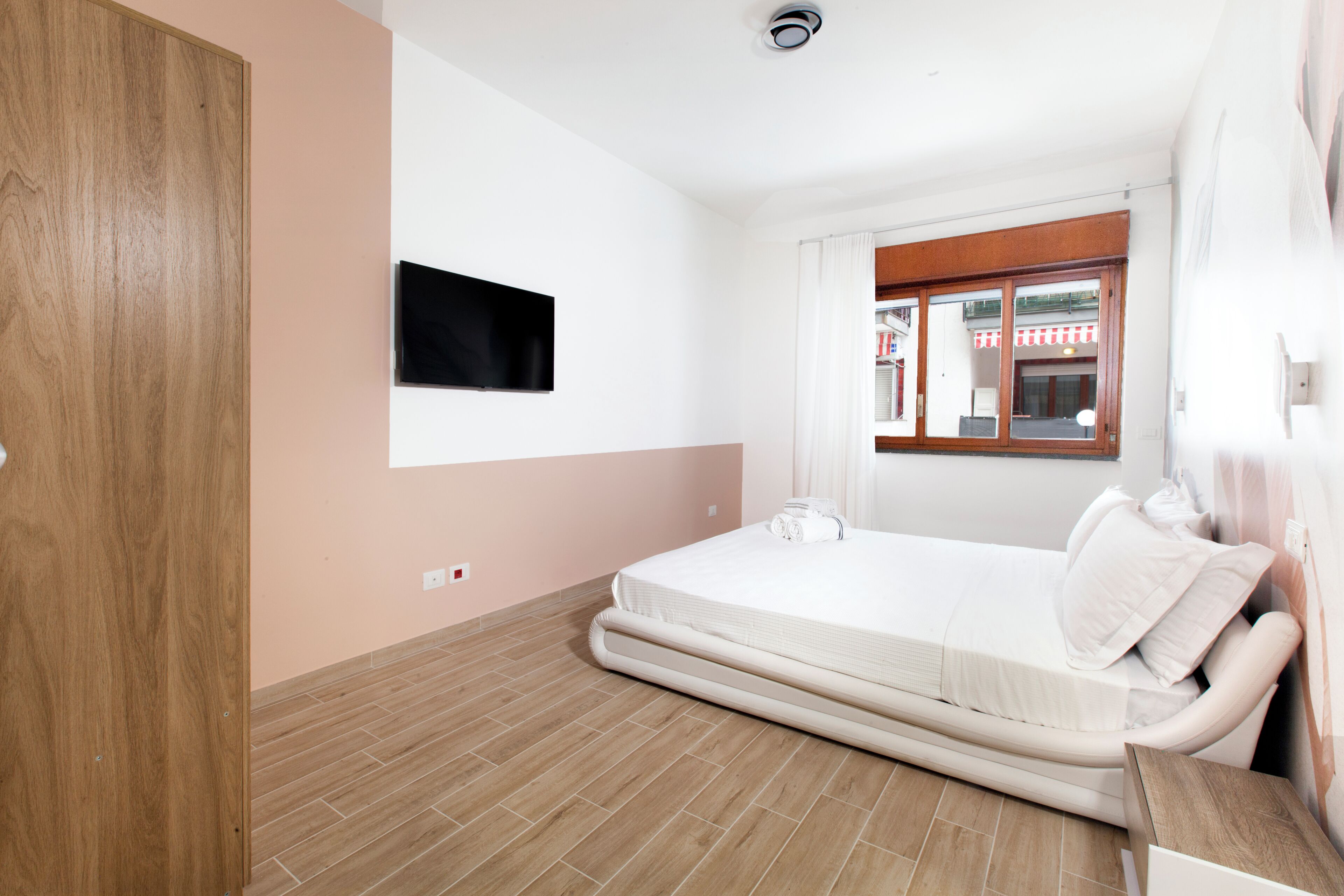 A bedroom with a bed, a television mounted on the wall, and a window with curtains.