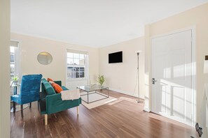 A modern living room with a sofa, a glass coffee table, a TV, and a door. - Cosy 1 bed Flat in Greenwich With Private Garden (London)