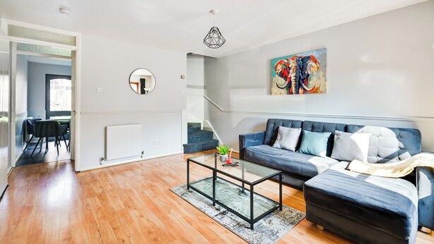 A modern living room with a glass coffee table, a blue sofa, a painting of an elephant, and a staircase leading to another room. - Apartment Sleeps 5 With Garden (London)