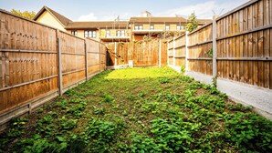 A fenced backyard with a grassy area and a building in the background. - Apartment Sleeps 5 With Garden (London)