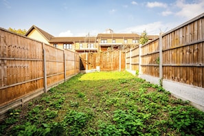 Ein umzäunter Garten mit Rasenfläche und einem Gebäude im Hintergrund.