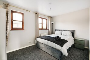 Ein Schlafzimmer mit einem Bett, zwei Fenstern, einem Nachttisch und einer Heizung.