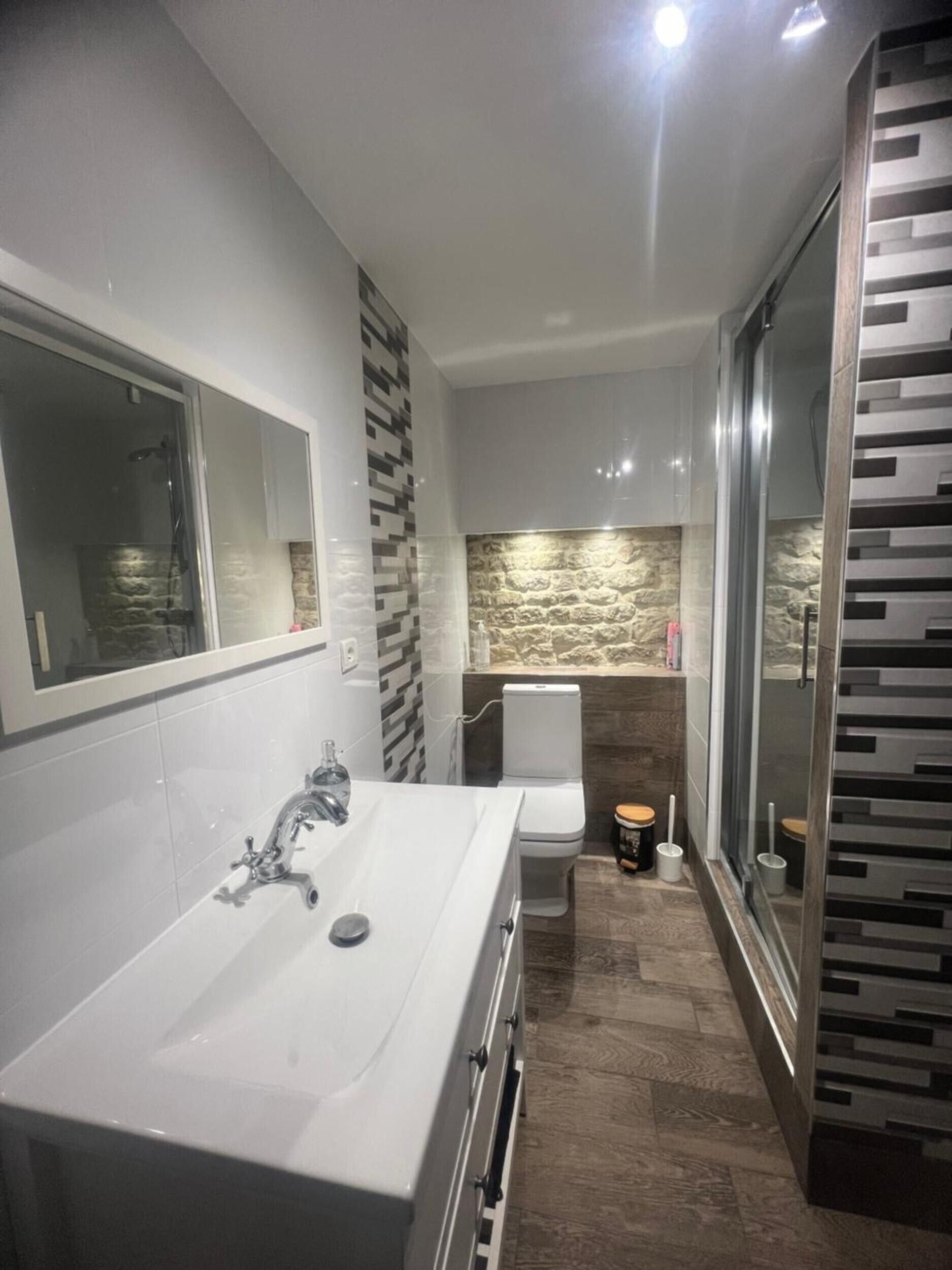 Un baño moderno con un lavabo blanco grande, cabina de ducha de vidrio, inodoro y espejo.