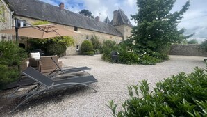 A stone building with a gravel courtyard, outdoor seating, and a large tree. - Apartment 'Gîte 1' with Shared Terrace, Shared Garden and Wi-Fi (Carentan-les-Marais)