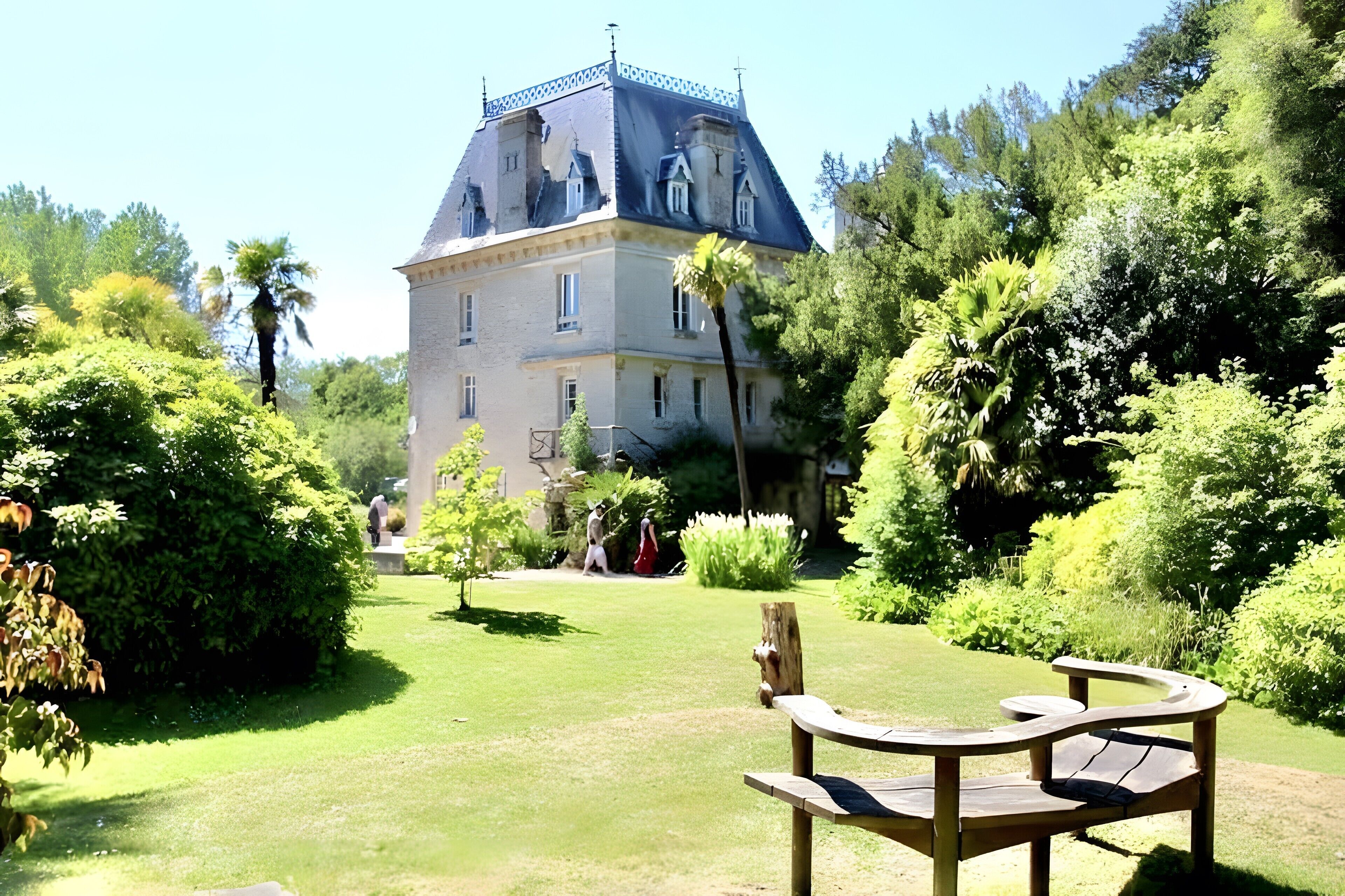A large, historic building with a prominent tower and multiple windows, surrounded by lush greenery and a well-maintained lawn.
