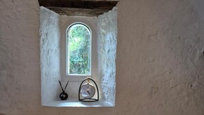 Una piccola finestra rustica con orologio e portacandele, una parete strutturata e un caldo elemento illuminante.