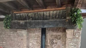 Un camino in pietra con una stufa a legna nera, una pianta verde sul ripiano e un divano bianco in primo piano.