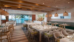 A restaurant with multiple dining tables, wicker chairs, and hanging light fixtures. - Award-Winning Beachfront Resort Penthouse | Pools, Dining & Kite Beach (Cabarete)