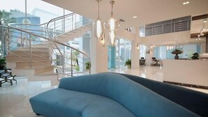 A modern lobby with a curved blue sofa, a spiral staircase, and a reception desk. - Award-Winning Beachfront Resort Penthouse | Pools, Dining & Kite Beach (Cabarete)