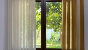 Una ventana con persianas verticales y vistas a follaje exterior.
