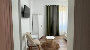 Una sala de estar moderna con un televisor de pantalla plana, un sofá blanco, una mesa de centro redonda y una cortina verde.