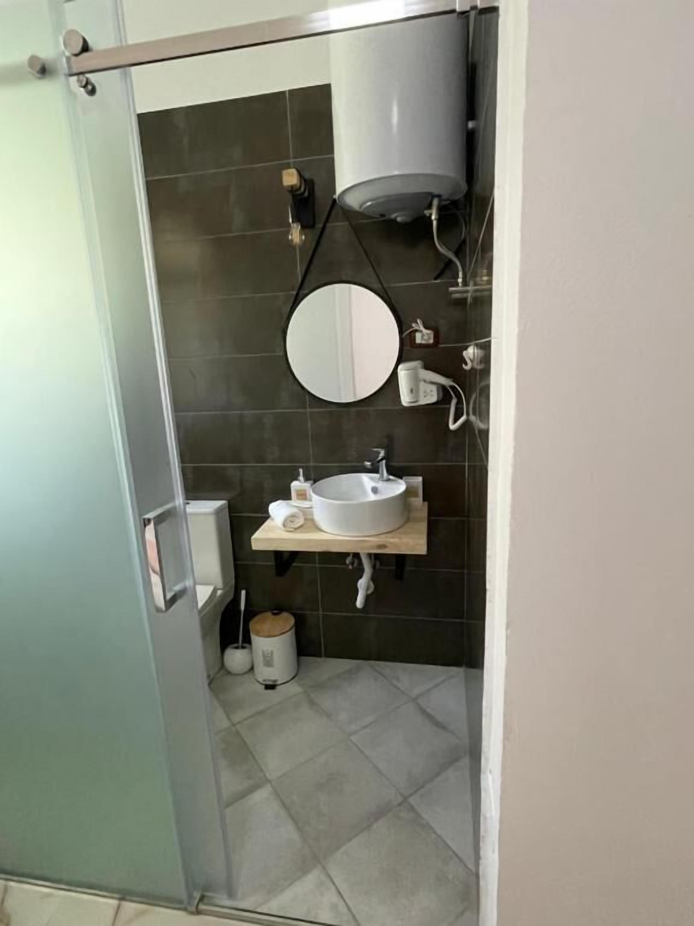 A bathroom with a toilet, sink, mirror, and a towel dispenser.