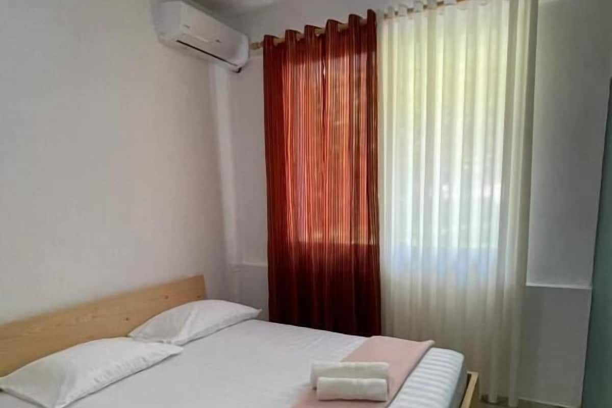 Uma cama de solteiro com roupa de cama branca, cabeceira de madeira e manta rosa.