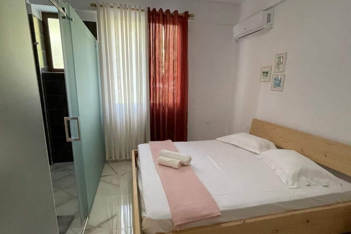 Quarto com cama, janela com cortinas, porta e aparelho de ar condicionado.