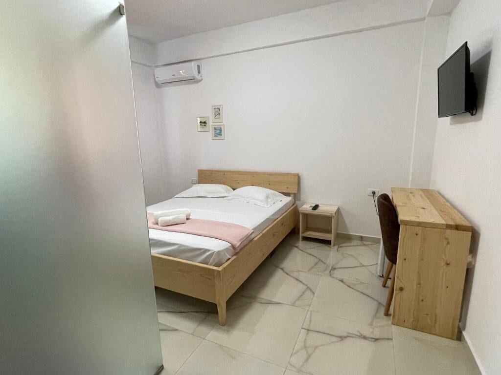 Une chambre à coucher avec un lit en bois, une table de chevet, un téléviseur fixé au mur et un bureau en bois.