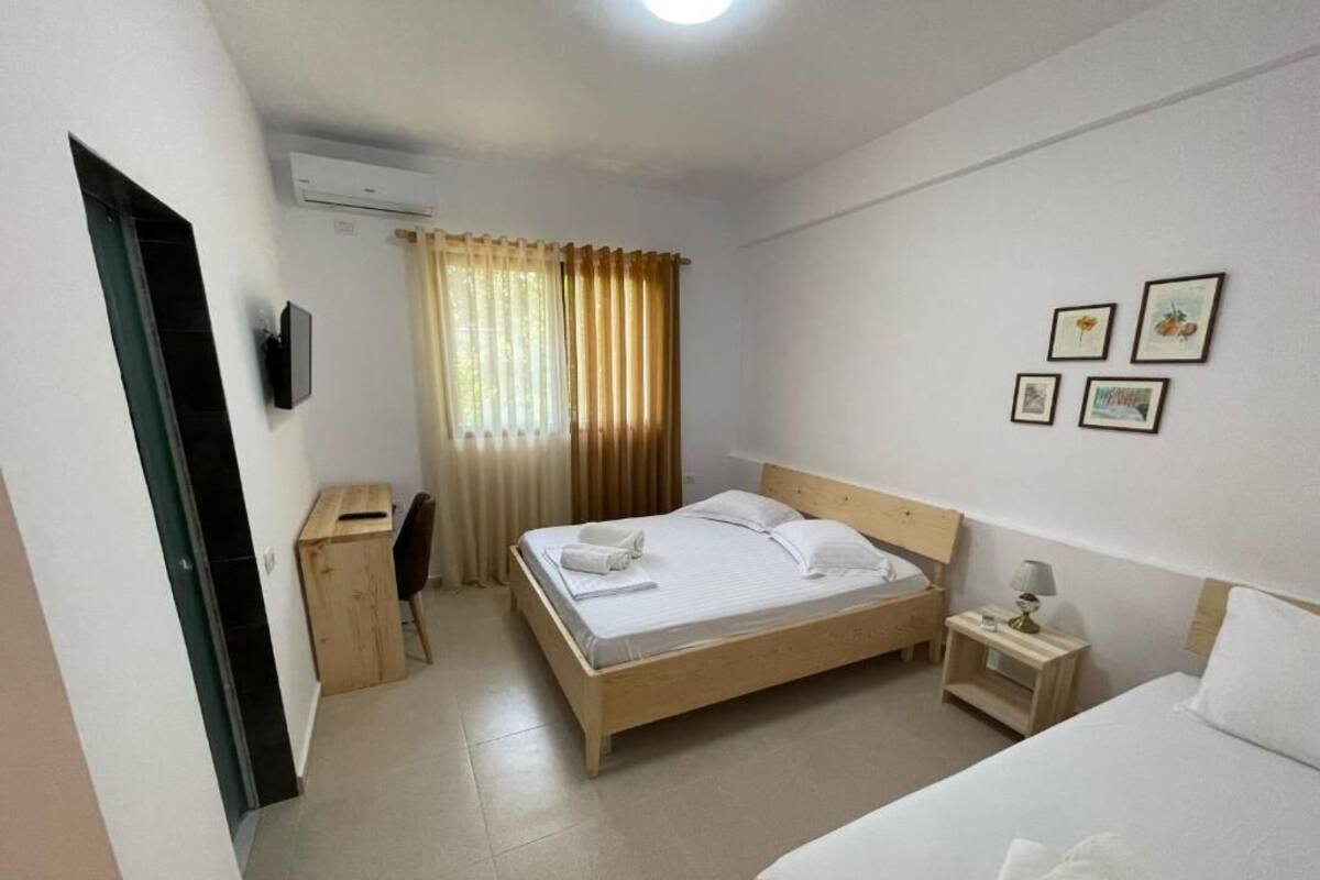 Quarto de hotel com cama, mesa de cabeceira, escrivaninha, cadeira e televisão.