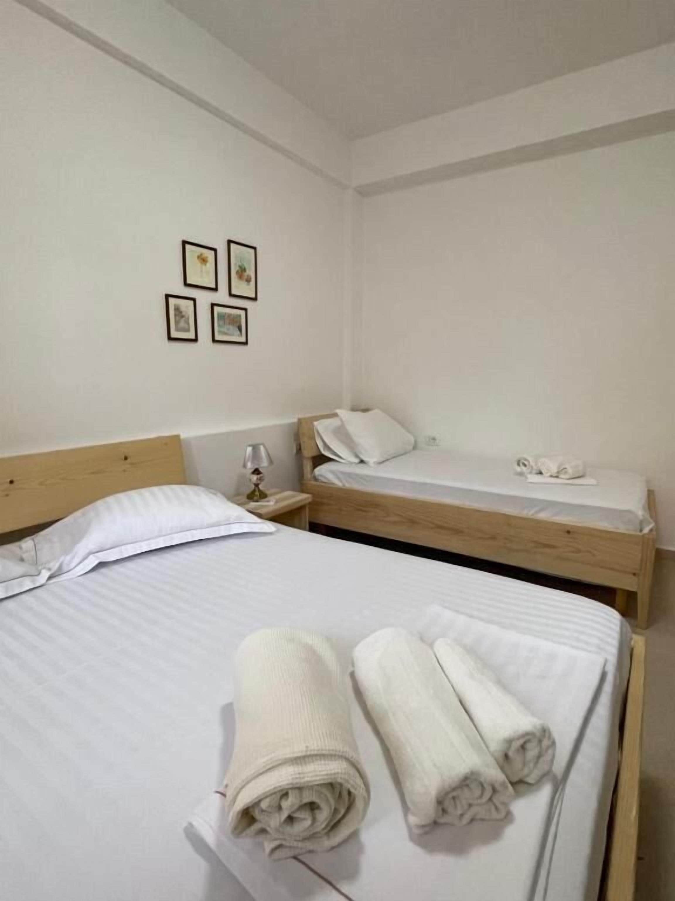 A bedroom with two beds, a nightstand, a lamp, and four framed pictures on the wall.
