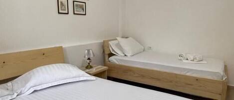 A bedroom with two beds, a nightstand, a lamp, and four framed pictures on the wall.