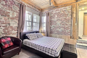 Ein Zimmer mit einem Bett, einem Stuhl, einem Fenster und einer Ziegelwand.