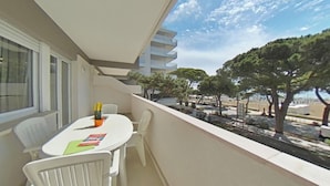 Een balkon met een witte tafel en stoelen, een kleine oranje container, en uitzicht op een straat met bomen.