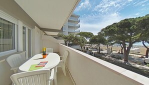A balcony with a white table and chairs, a small orange container, and a view of a tree-lined street. - Wide Sea-front Apartment-10 Metres From the Beach (Lignano Sabbiadoro)