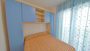 A bedroom with a bed, a wardrobe, and a window with curtains. - Wide Sea-front Apartment-10 Metres From the Beach (Lignano Sabbiadoro)