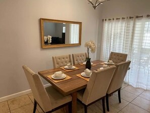 A dining area with a wooden table, beige upholstered chairs, a vase with flowers, and a mirror on the wall. - Storey Lake 4BR Retreat, Private Pool, Sleeps 10 (Kissimmee)