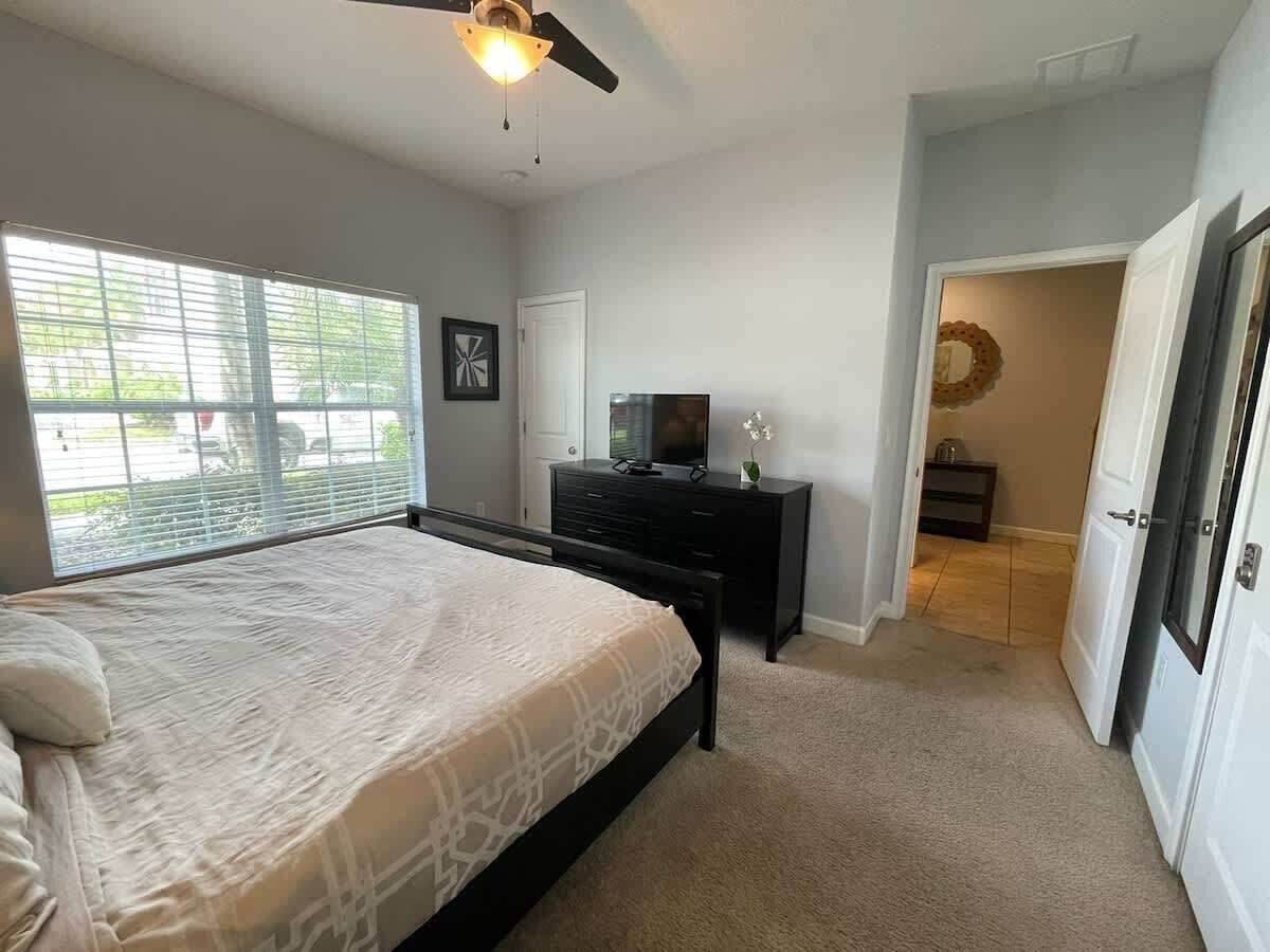 Een slaapkamer met een bed, een dressoir, een televisie en een plafondventilator.