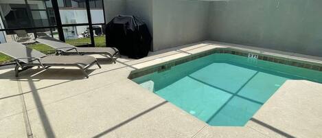 Una piscina con sillas de descanso y una zona de barbacoa cubierta.