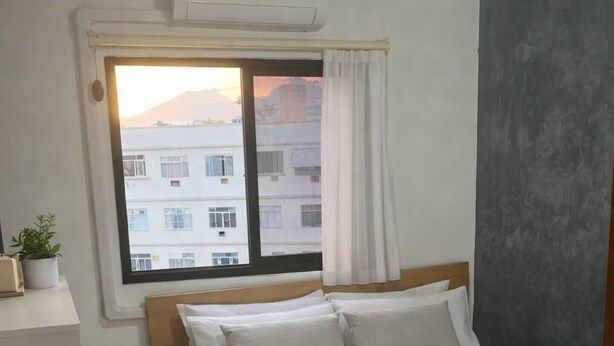 Een slaapkamer met een bed, een raam met gordijnen, een plafondventilator en een airconditioning.