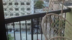 Een balkon met uitzicht op een stadsgezicht tijdens zonsondergang, een hangstoel en geparkeerde auto's eronder.