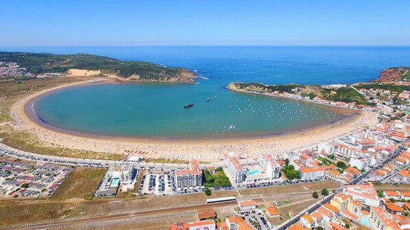 An aerial view of a coastal town with a beach, buildings, and a clear sky.