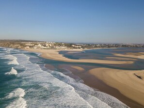 Une vue aérienne d’une zone côtière avec une plage, des vagues et une ville en arrière-plan.