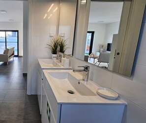 A modern bathroom with two sinks, a large mirror, and a potted plant.