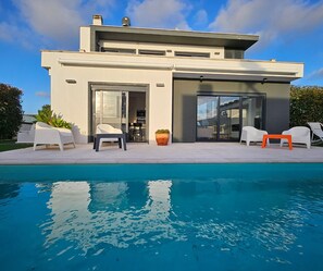 A modern house with a swimming pool, outdoor seating, and a large sliding glass door.