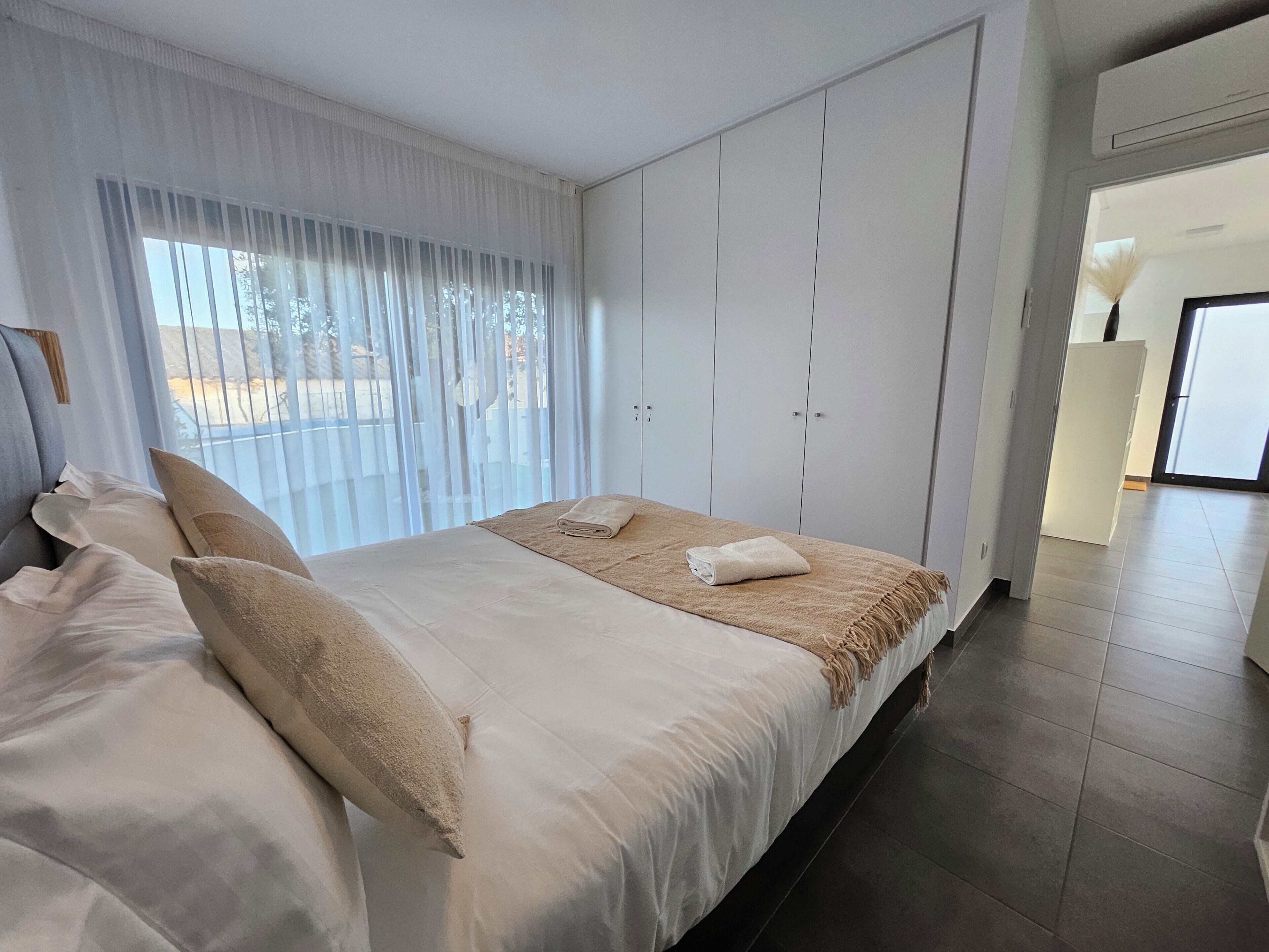 A bedroom with a bed, curtains, a wardrobe, and a view through the window.