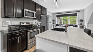 Une cuisine moderne avec des meubles de couleur sombre, des appareils en acier inoxydable, un grand îlot central et une vue sur l’extérieur.