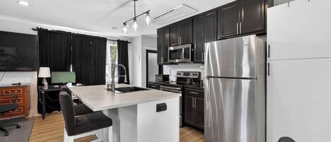 A modern kitchen with a central island, stainless steel appliances, and dark cabinetry.