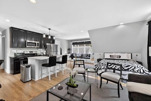 A modern apartment with a kitchen, dining area, and a bedroom with a zebra print bedspread.